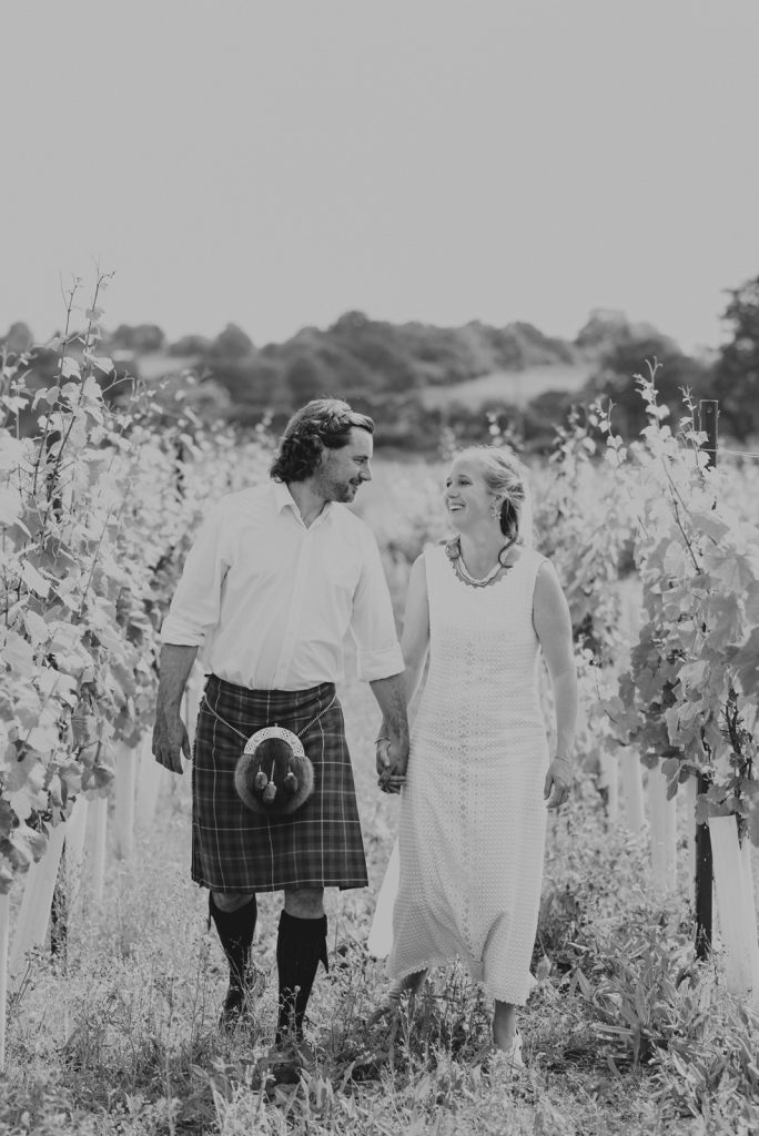 a bride and a groom walking in an English vineyard